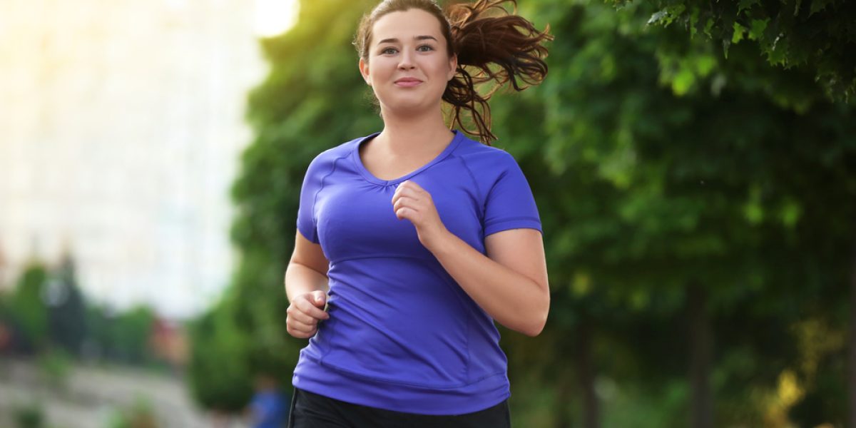 Jeune femme en surpoids courant dans la rue, pratiquant du jogging pour rester active et tonique.